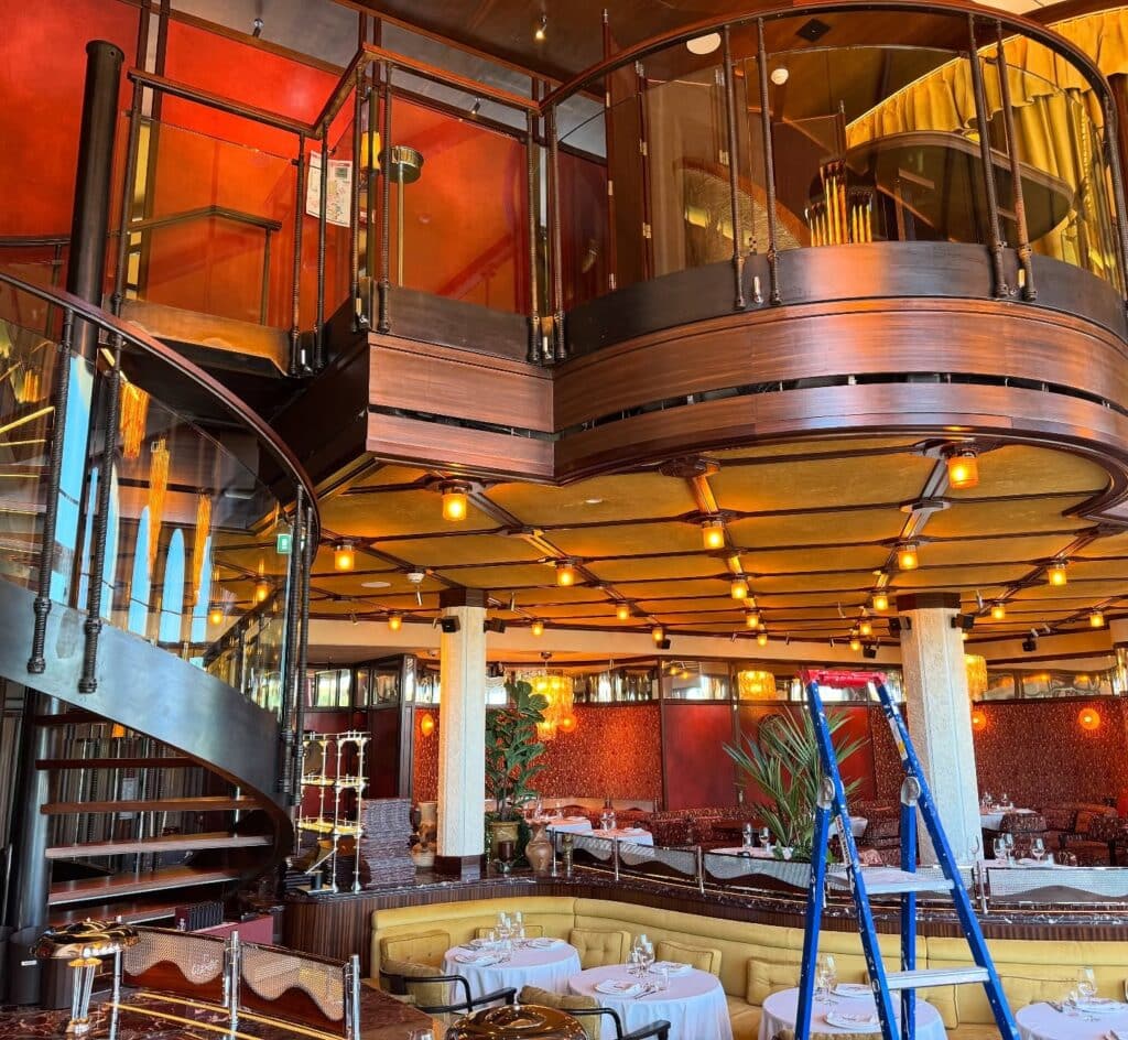 Restaurant Luxe : Design Intérieur et Escalier Métallique Intérieur luxueux de restaurant avec escalier en colimaçon, mezzanine en bois sombre et banquettes jaunes, échelle bleue au premier plan.