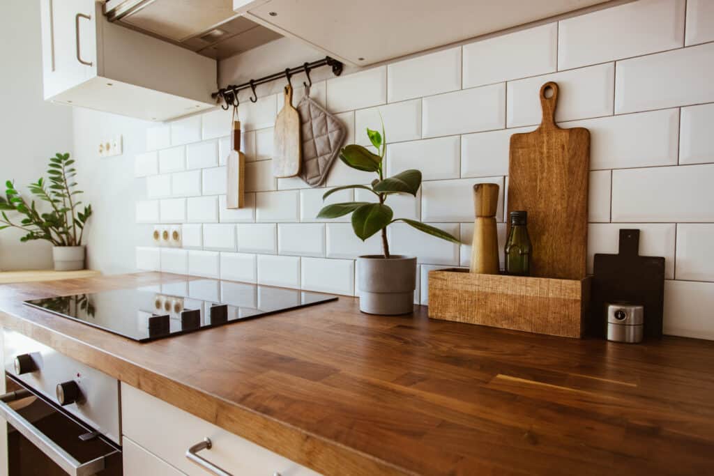 Plan de travail bois foncé cuisine moderne avec plaque vitrocéramique, carreaux métro blancs et ustensiles suspendus.